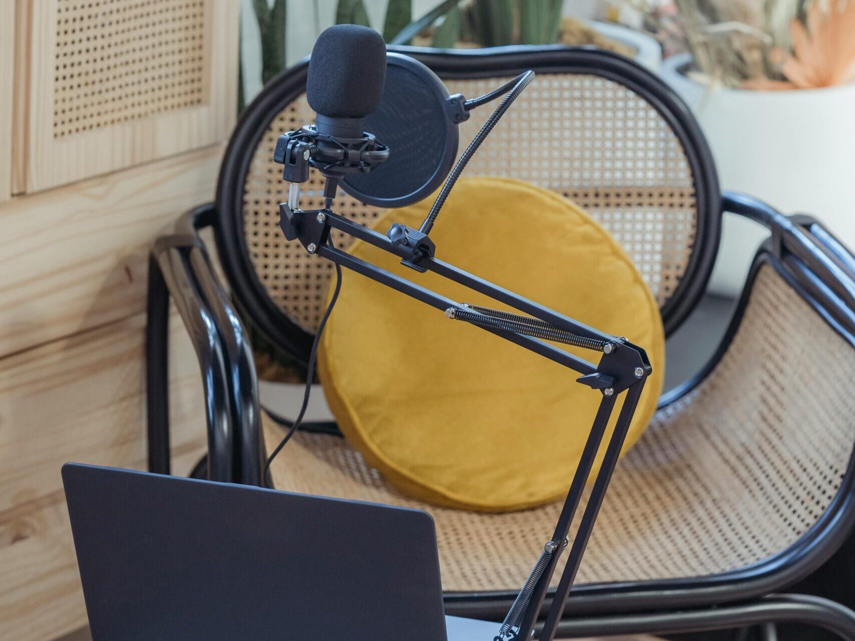 Modern laptop and microphone on tripod placed near wicker chair in modern studio before recording podcast